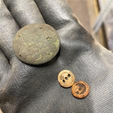 An 18th/19th-century gilt coat button and two bone buttons. The coat button may have been lost by someone walking through the graveyard. The bone buttons were found on the chest bone of a burial and reveal that the person was buried wearing a shift or a shirt.
