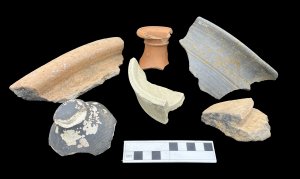 Image 4. Examples of Roman pottery from Leicester Cathedral. Clockwise from top left: the rim of a shell-tempered ware jar, the neck and rim of an oxidized ware flagon, part of a greyware jar (probably made locally), the rim of the dolium, an imported mortarium from Gaul and the base of a colour coated ware beaker (upside down) from the Nene Valley. Image: ULAS